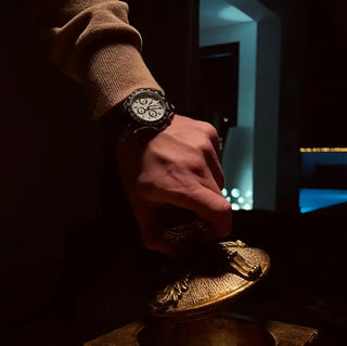 Hand wearing a black watch pouring from a decorative golden teapot.